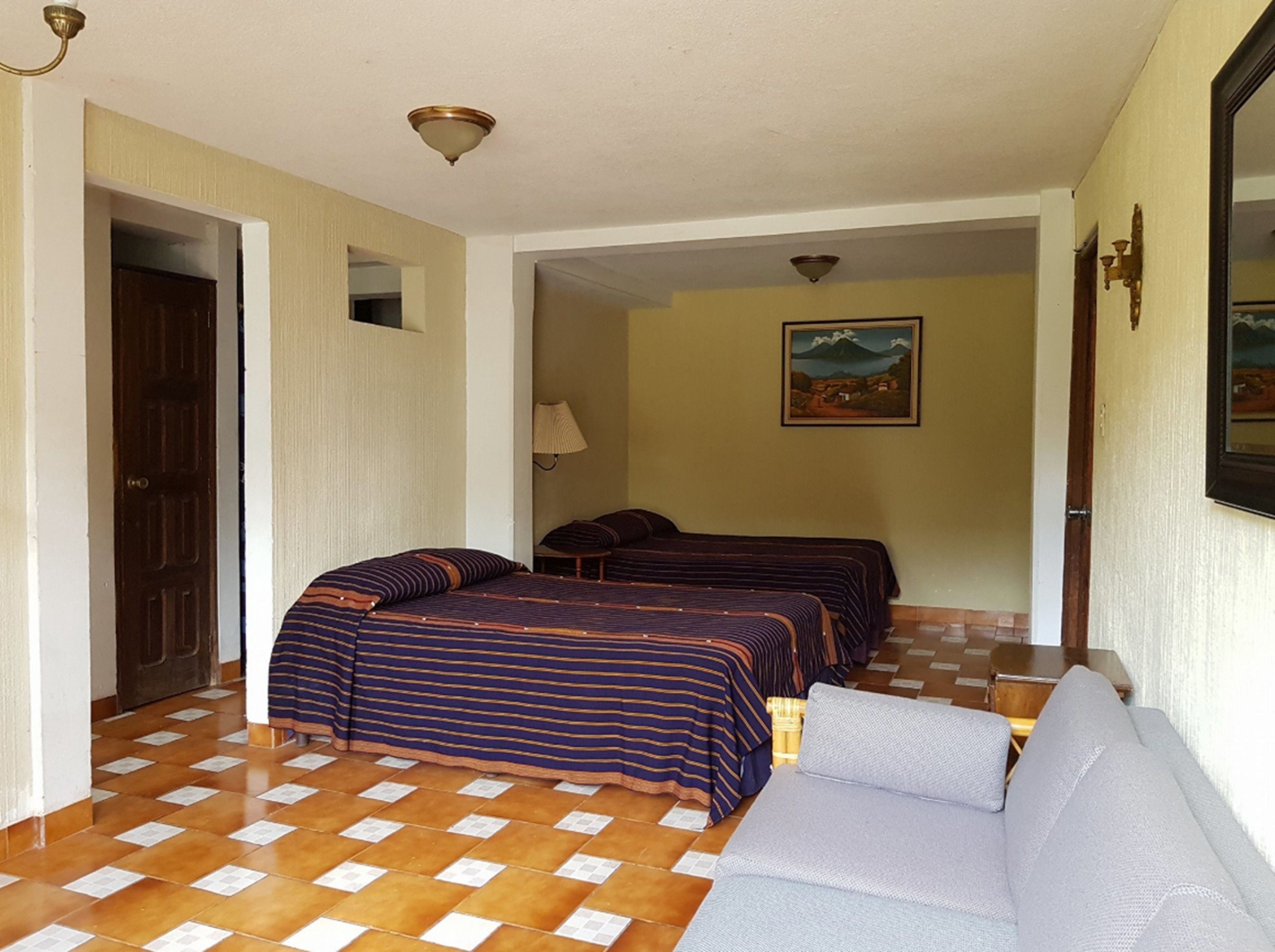 A hotel room with two beds, a sofa, a painting on the wall, and a door.