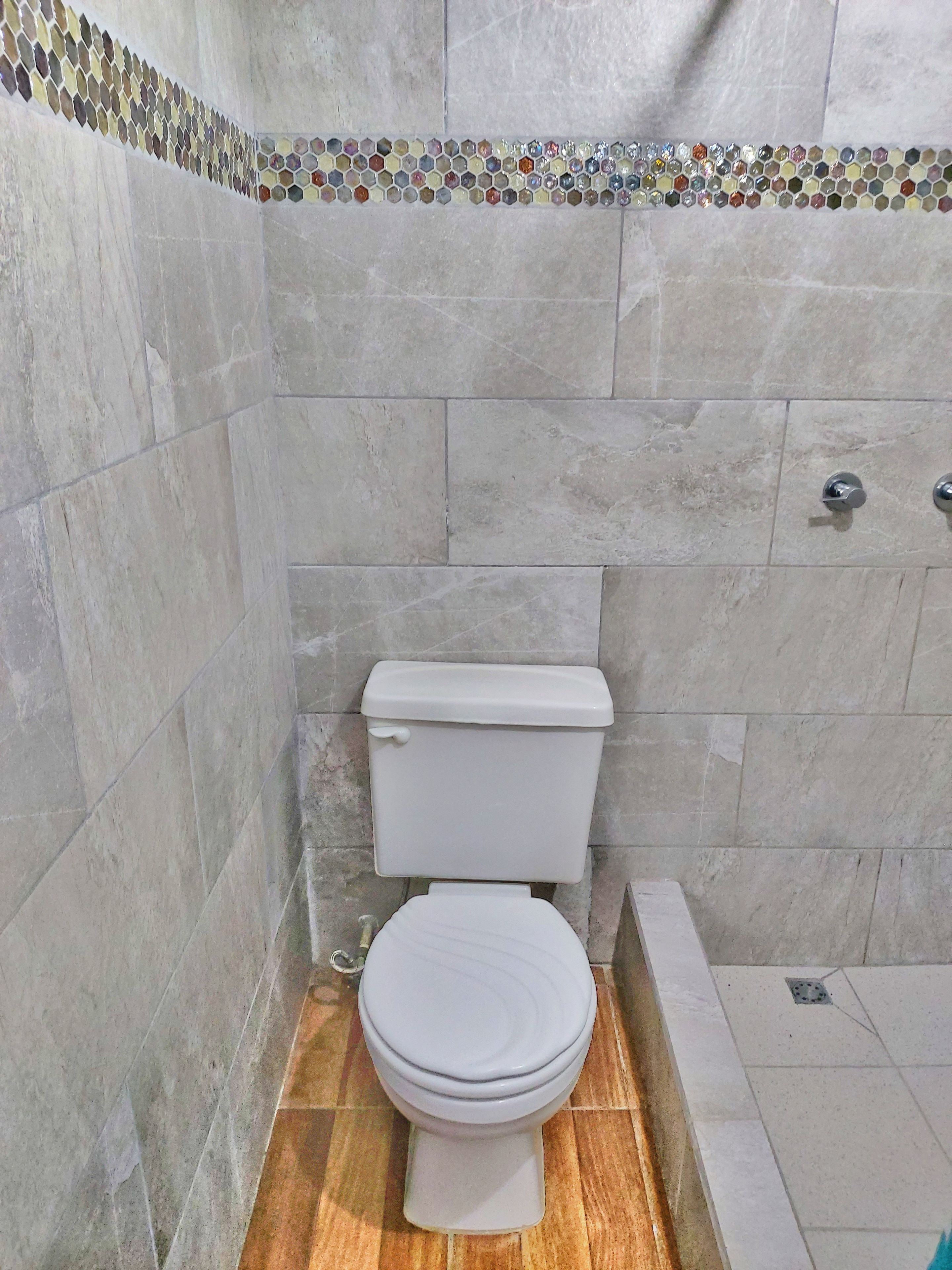 Ein Badezimmer mit Toilette, Dusche und Fliesenboden.