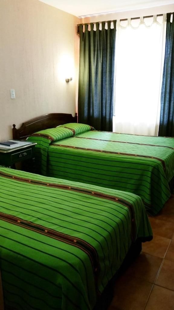 A hotel room with two beds, a nightstand, and a window with curtains.