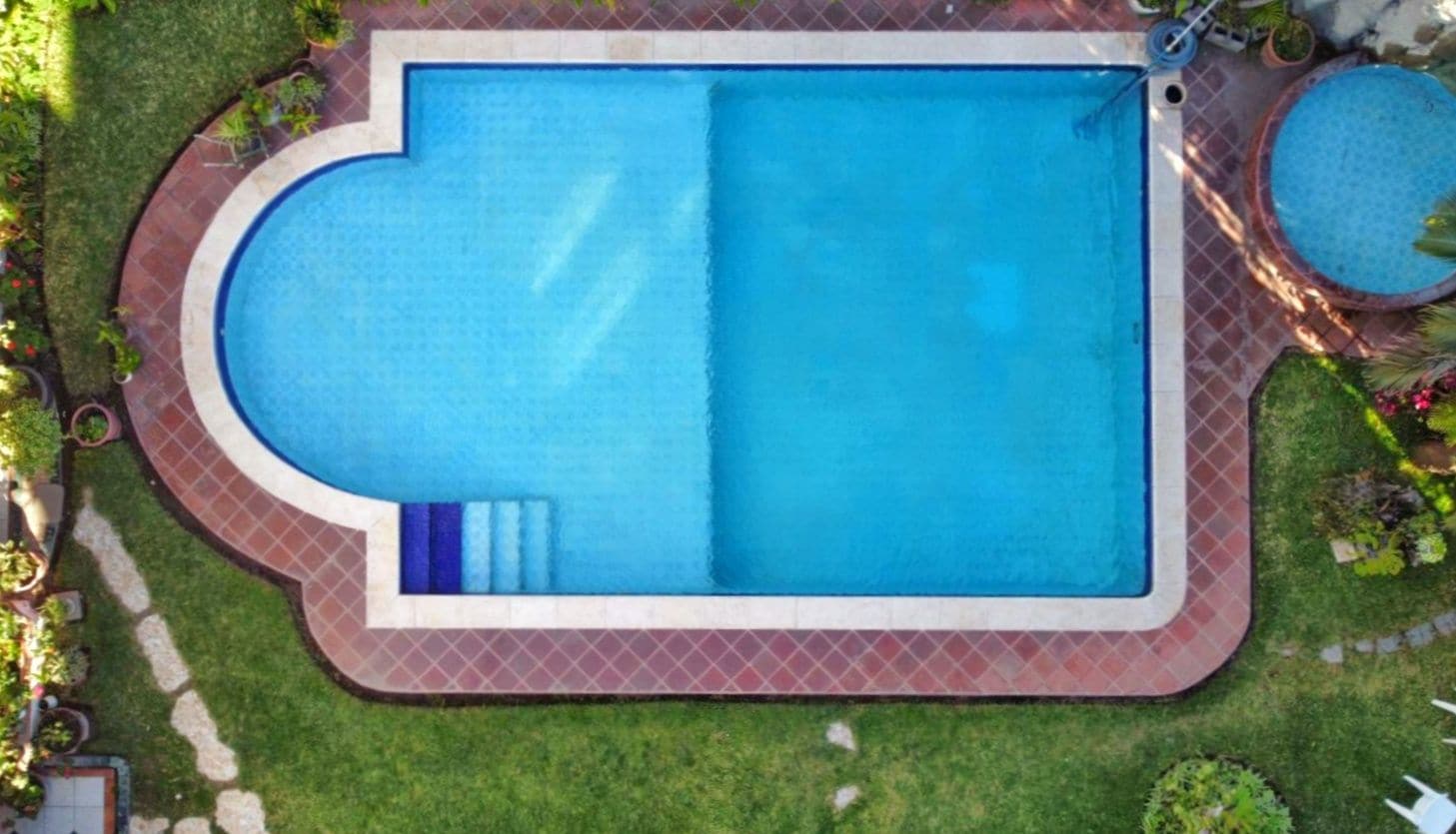 A rectangular swimming pool with a curved edge, surrounded by a brick border and a grassy area.