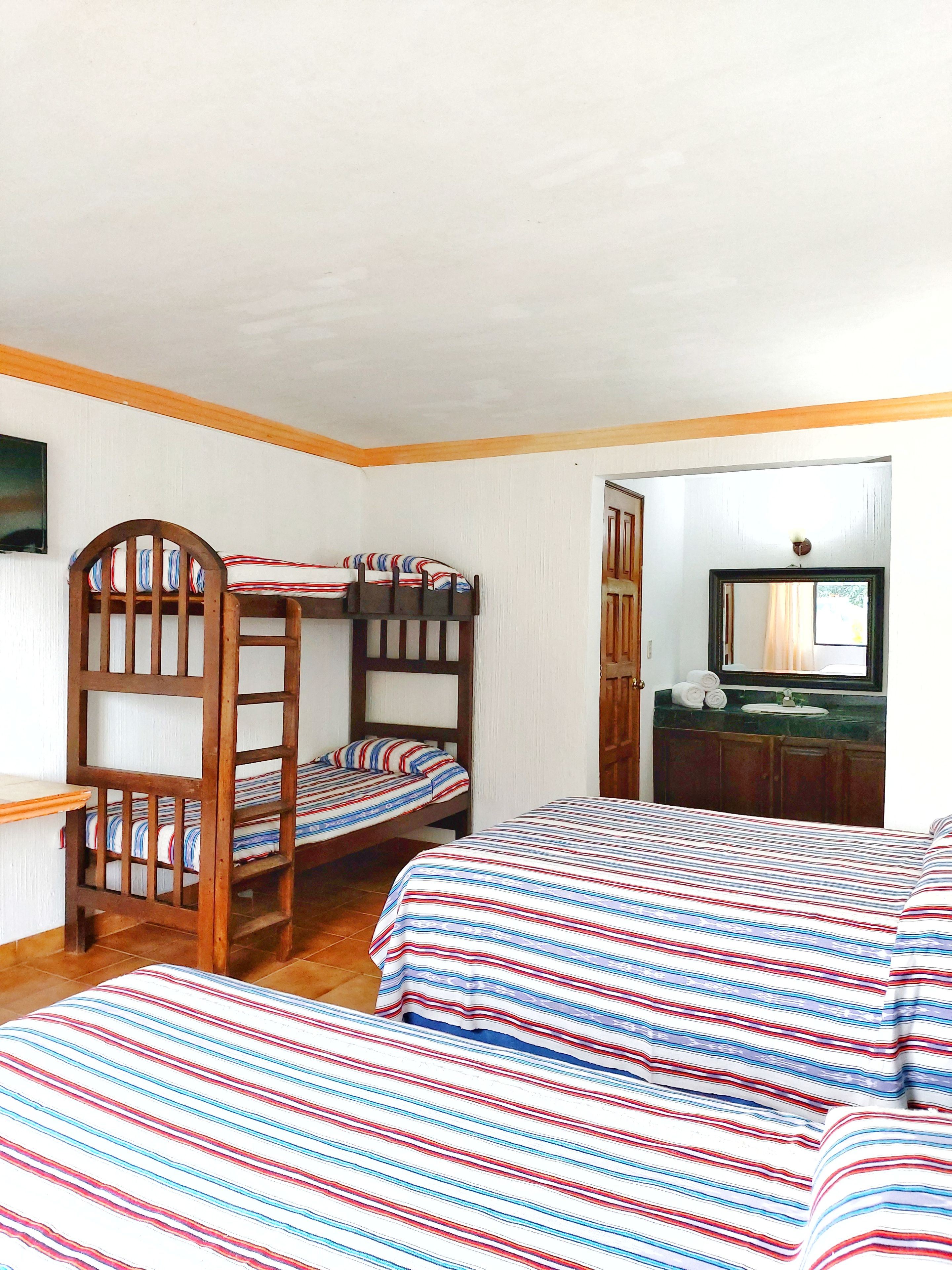 A room with bunk beds, a wooden headboard, a small desk, and a bathroom with a mirror and sink.