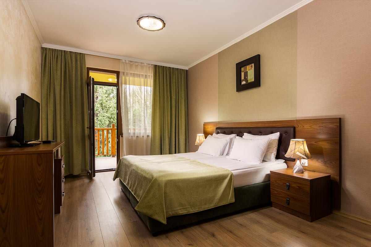 A hotel room with a bed, bedside table, lamp, and a television on a wooden dresser.