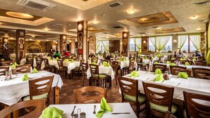 A spacious restaurant with multiple dining tables and chairs, featuring a rustic interior with exposed brick walls and wooden beams. - Hotel Elbrus SPA & Wellness (Velingrad)
