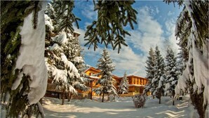 A snow-covered landscape with a lodge featuring a prominent building with a sloped roof and multiple windows. - Hotel Elbrus SPA & Wellness (Velingrad)