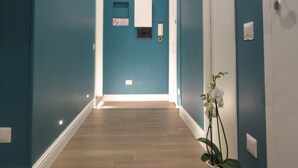 A hallway with blue walls, a potted plant, and a door at the end. - Gea Suite (Naples)