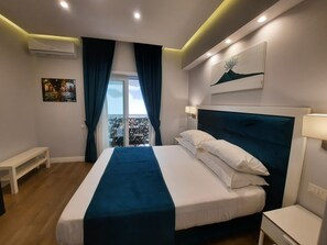 A modern hotel room with a large bed, a balcony with a view, a painting on the wall, and an air conditioning unit. - Gea Suite (Naples)