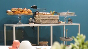 A buffet table with various pastries and a cake, a white plate, a white cup, and a spoon. - Gea Suite (Naples)