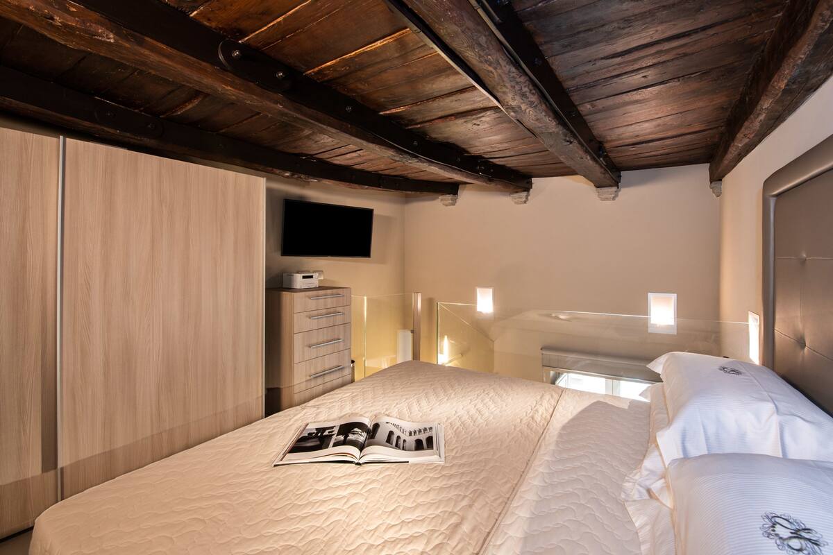 Ein Schlafzimmer mit Holzboden, einem Bett mit einer Zeitschrift, einem Schminktisch und einem an der Wand montierten Fernseher.