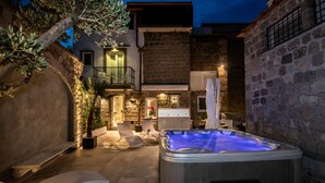 A hot tub in a courtyard with stone walls, a balcony, and lounge chairs. - Antica Dimora Magi (Sorrento)
