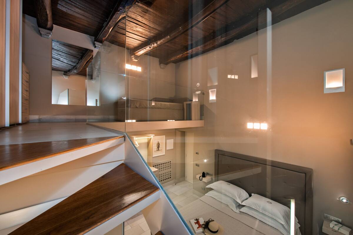 Ein modernes Hotelzimmer mit einer gläsernen Wendeltreppe, einem Bett mit weißen Leinentüchern und einem kleinen Nachttisch.