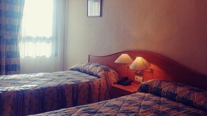 Een hotelkamer met twee bedden, elk met een beddeken met een patroon, een nachtkastje met een lamp en een ingelijst foto aan de muur.