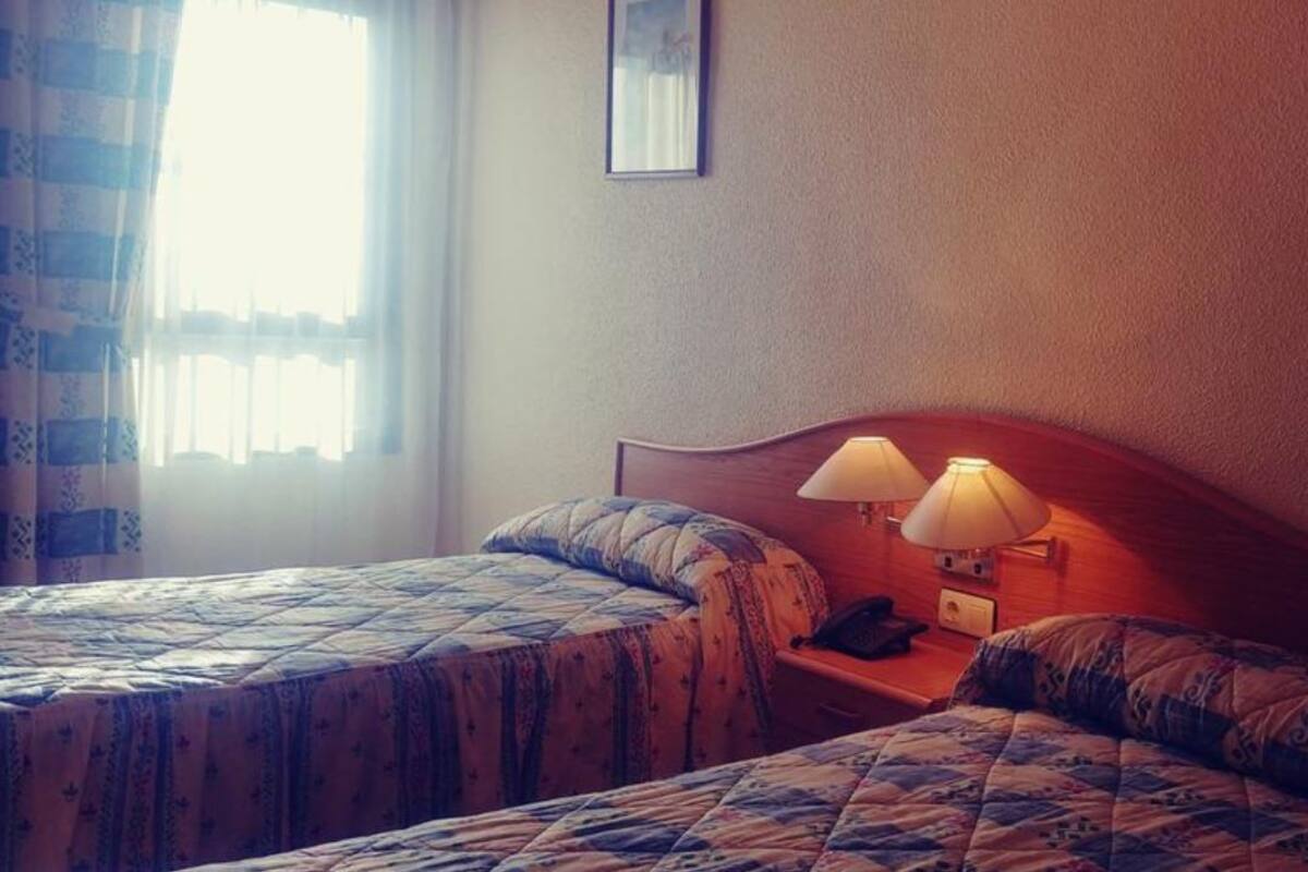 Une chambre d’hôtel avec deux lits, chacun recouvert d’une couvre-lit à motifs, une table de chevet avec une lampe et un tableau encadré au mur.