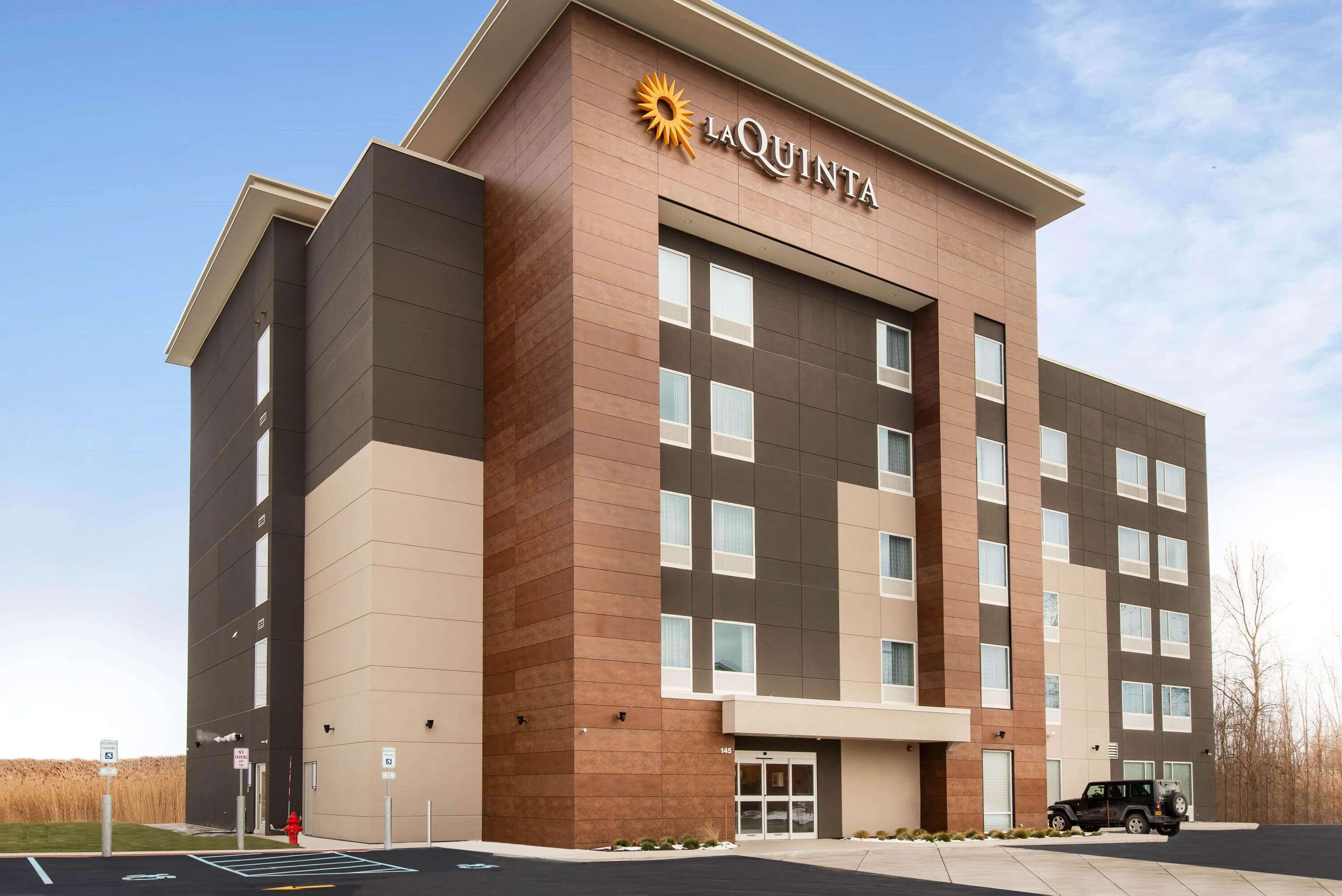 A La Quinta hotel with a modern design, featuring a prominent logo, multiple floors, and a parking area.