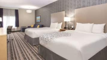 A hotel room with two beds, a desk, a chair, and a large window with curtains.