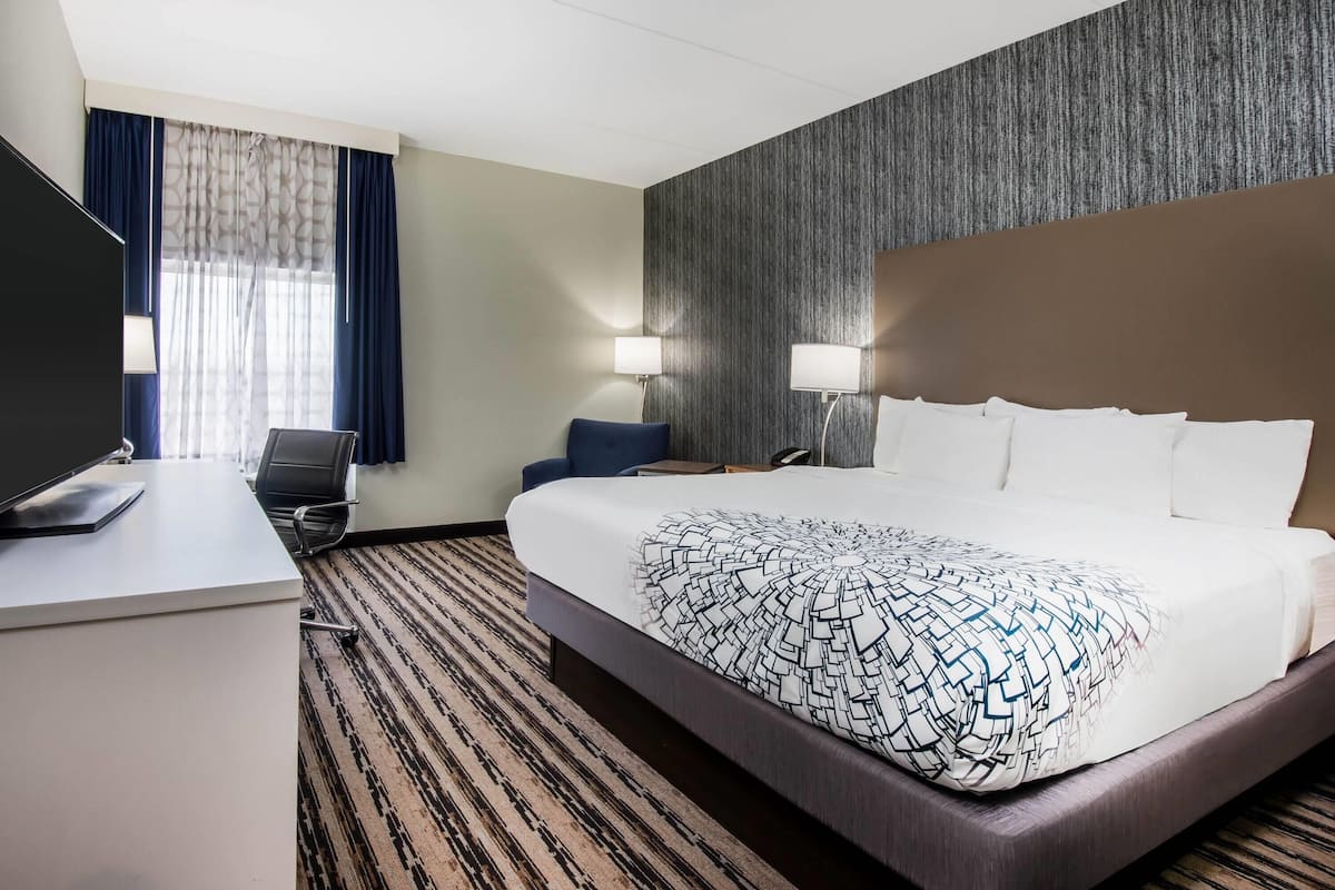 A hotel room with a large bed, a desk with a computer, a chair, and two bedside lamps.
