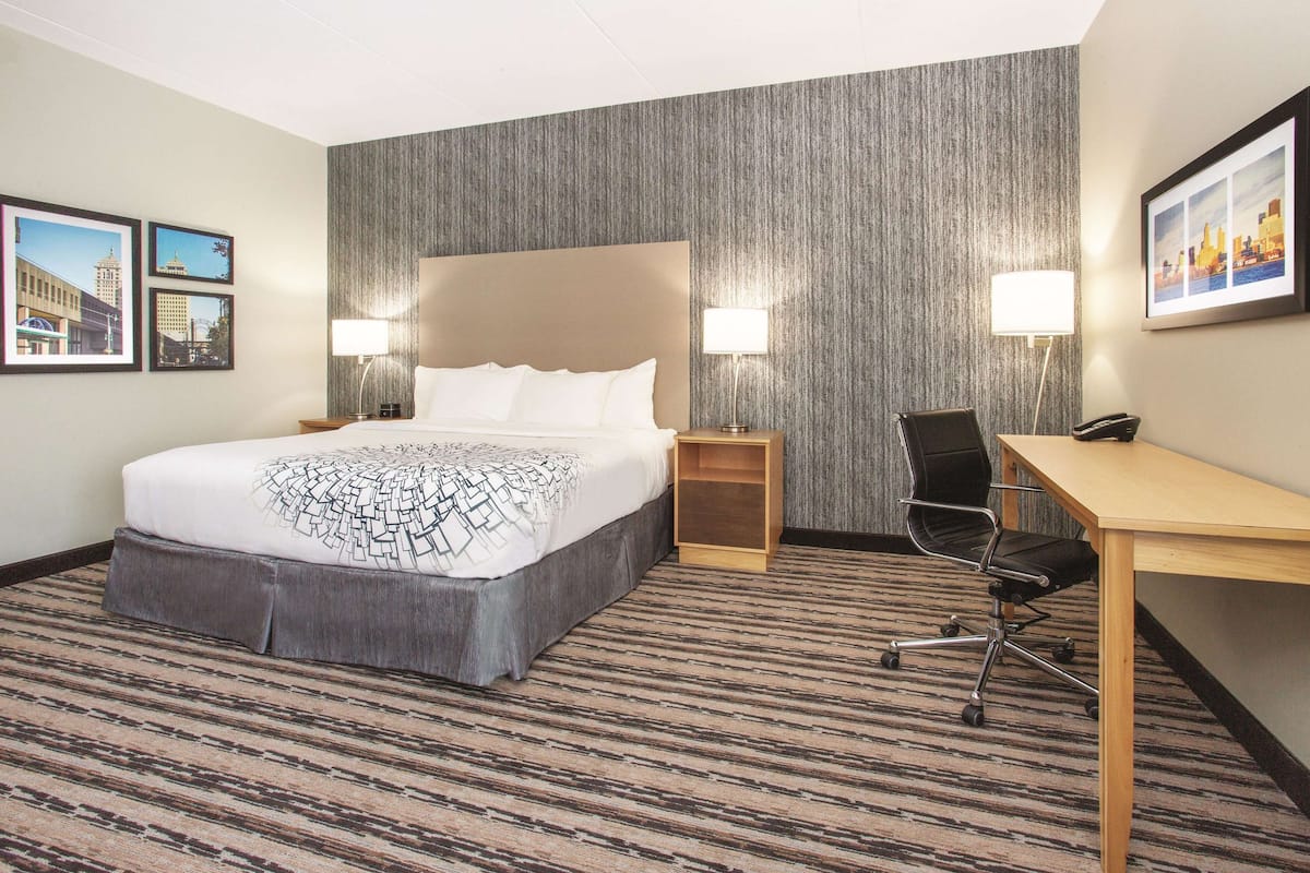 A hotel room with a large bed, a desk, two bedside lamps, and a carpeted floor.