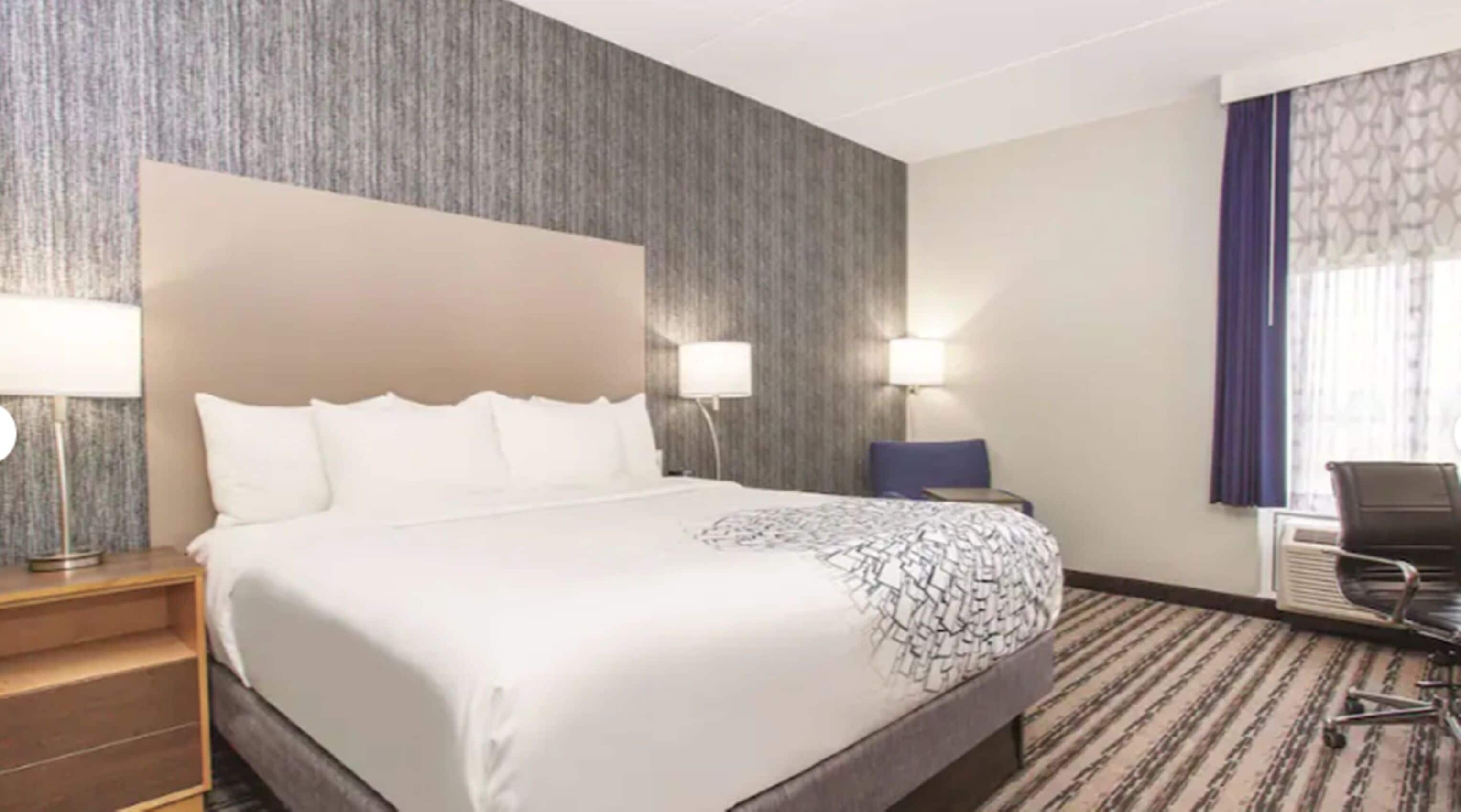 A hotel room with a large bed, two bedside lamps, a chair, a desk, and a window with curtains.