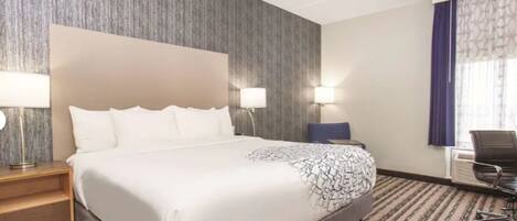 A hotel room with a large bed, two bedside lamps, a chair, a desk, and a window with curtains.