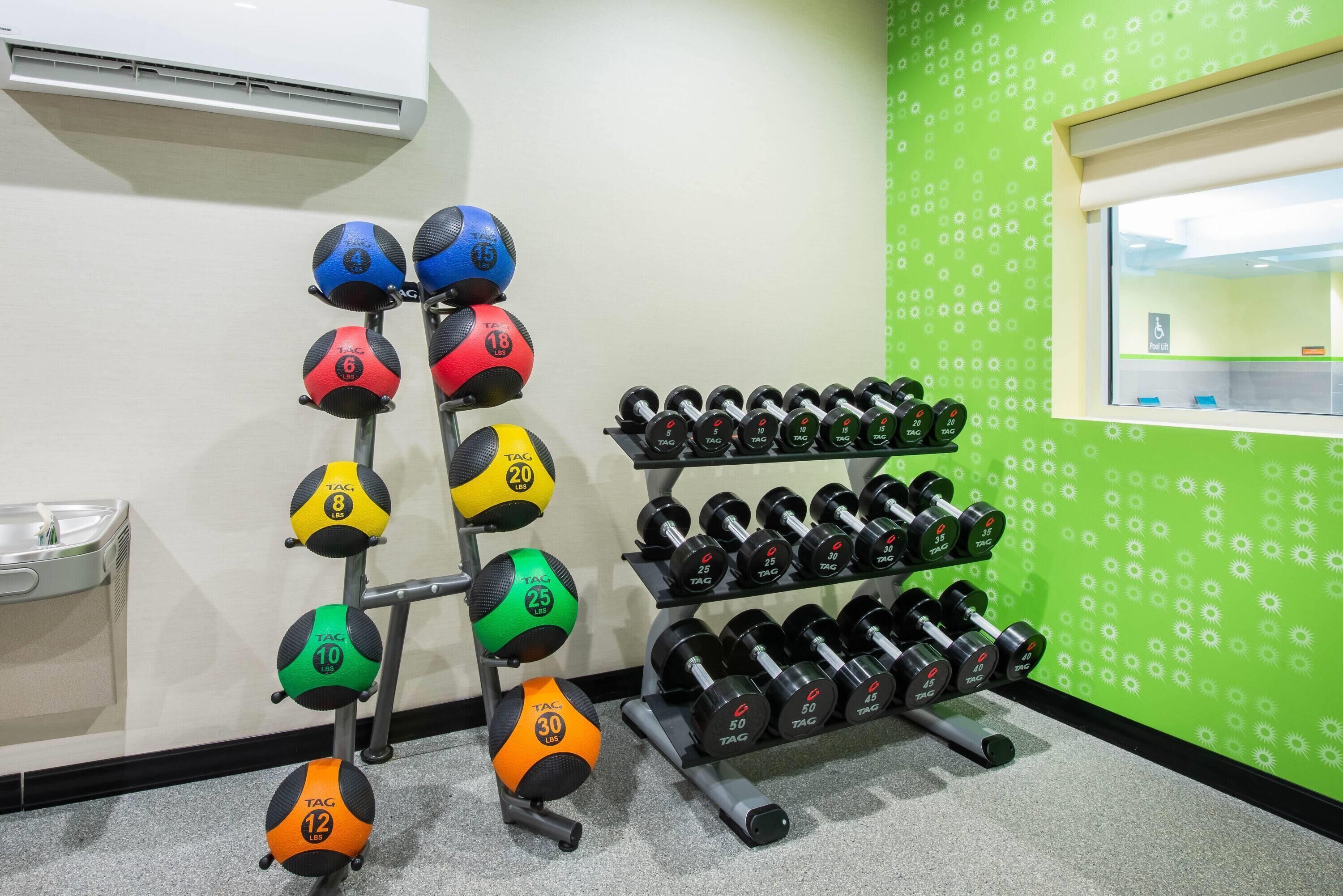 A gym with various exercise equipment, including dumbbells and medicine balls, arranged on racks.