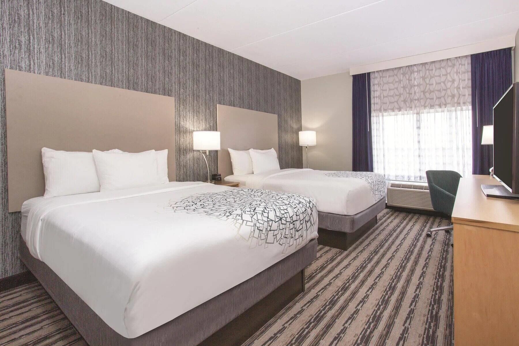 A hotel room with two beds, a desk, and a chair.