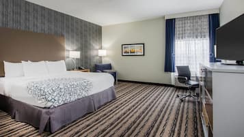 Une chambre d’hôtel avec un grand lit, un bureau avec une chaise, une télévision et une fenêtre avec des rideaux.