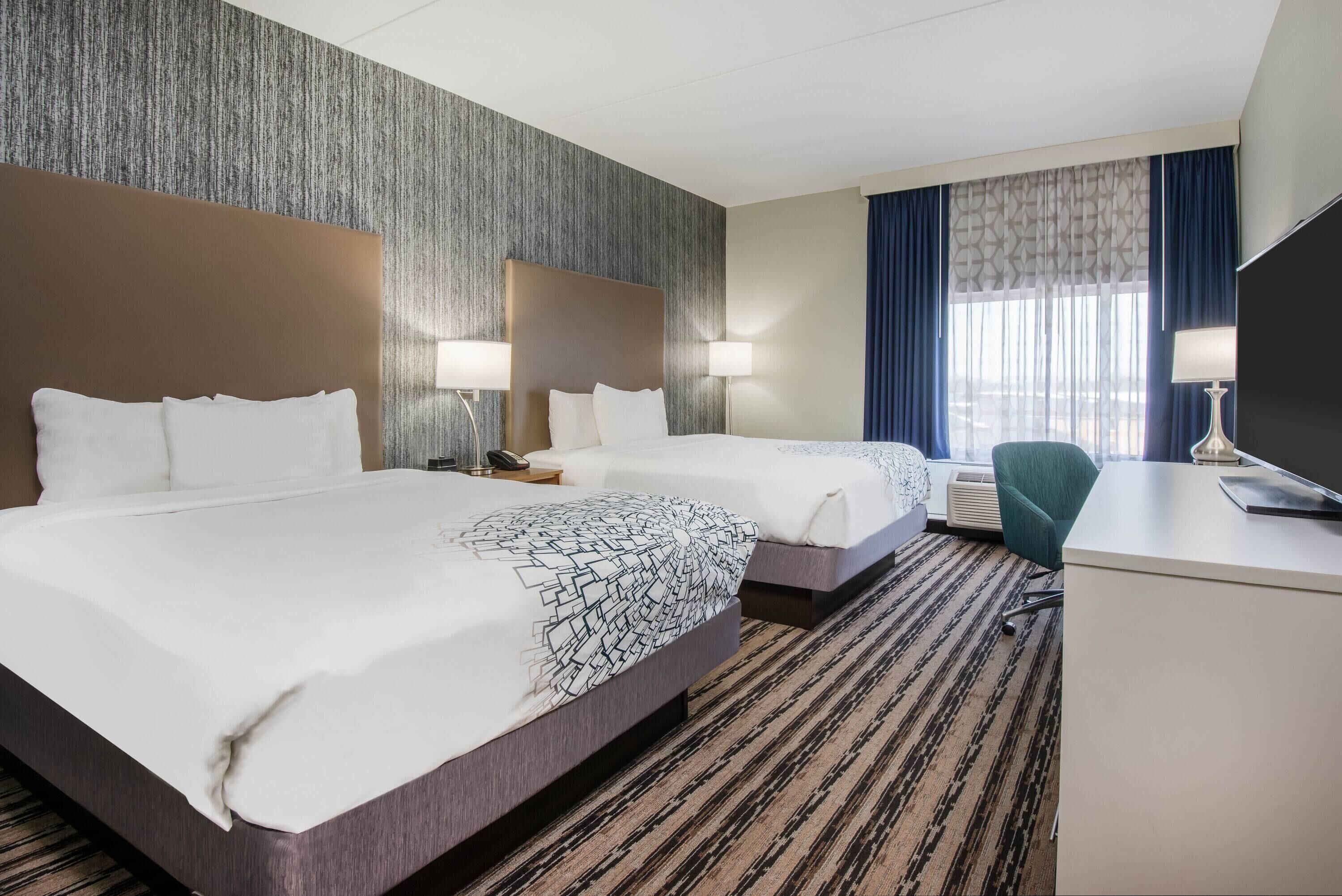 A hotel room with two beds, a desk, and a TV.
