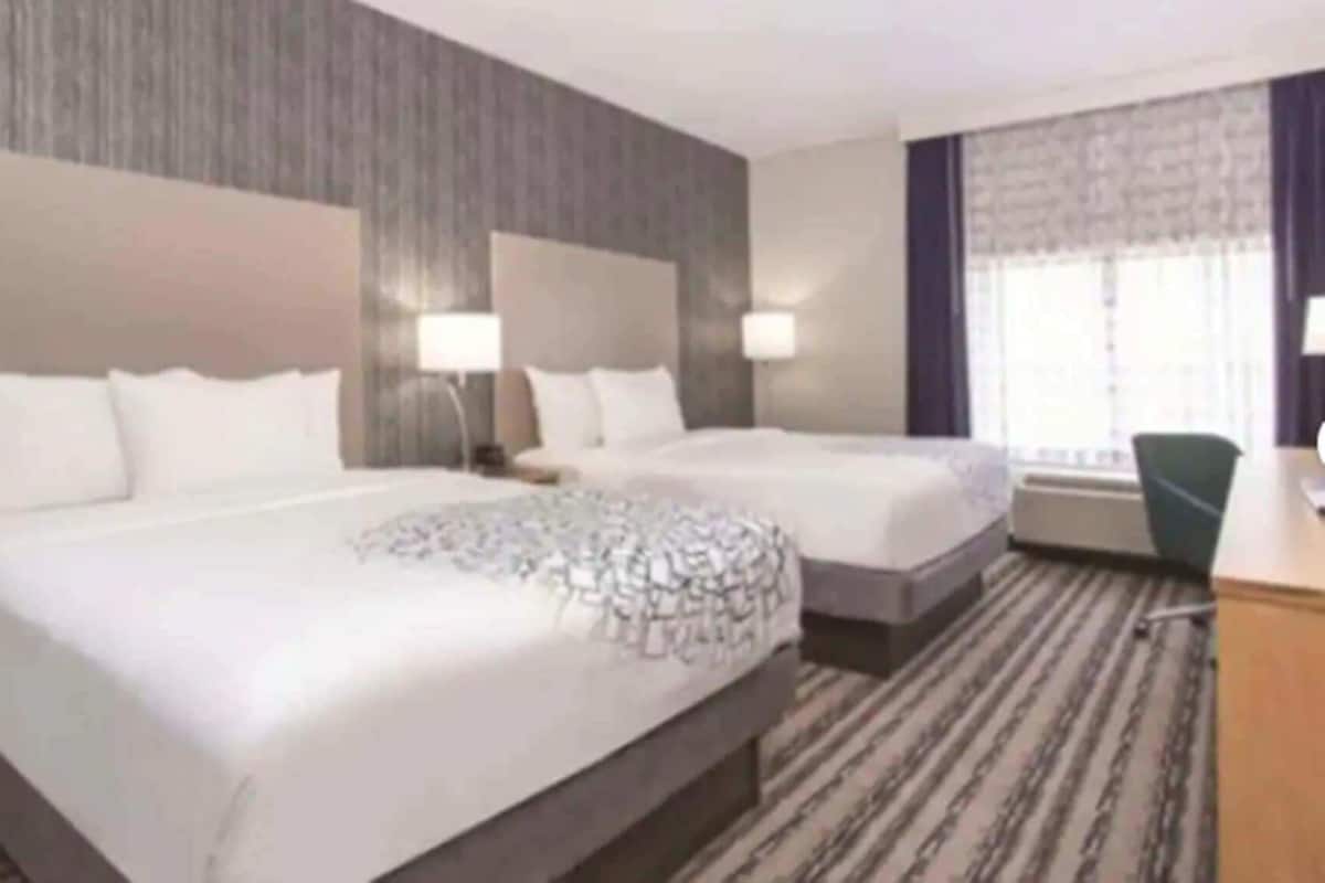 A hotel room with two beds, a desk, a chair, and a large window.
