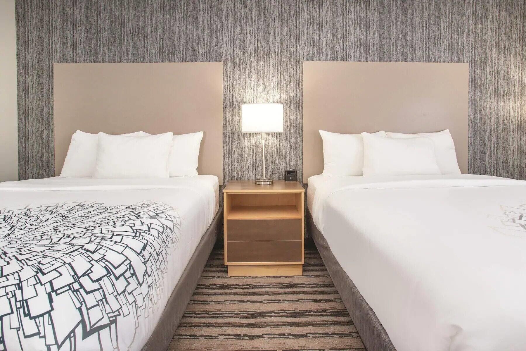 Une chambre d’hôtel avec deux lits, une table de chevet avec une lampe et un tapis à motifs.