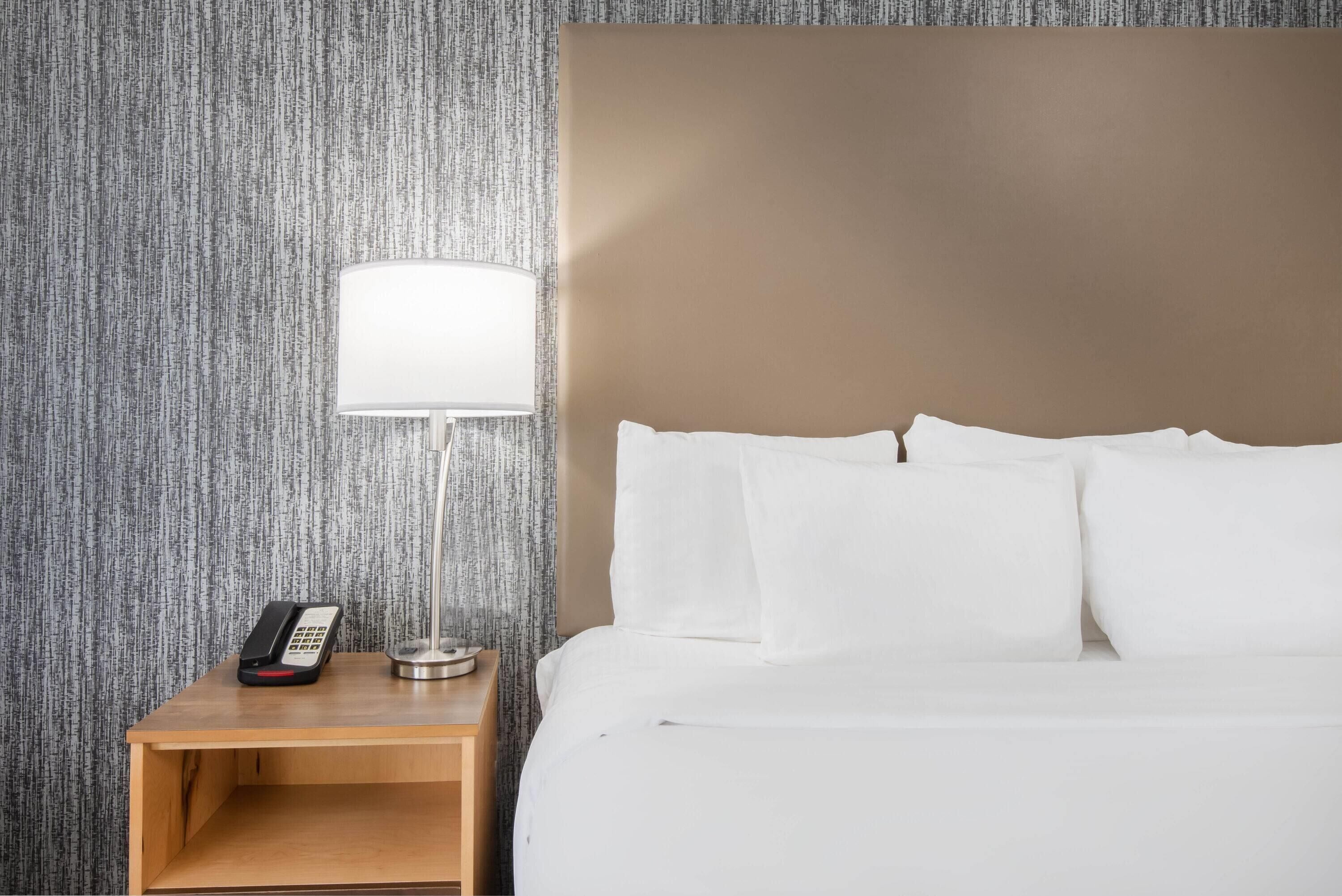 A hotel room with a bed, a bedside table with a lamp, and a telephone.