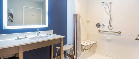 A bathroom with a large mirror, a sink, a shower with a glass door, and a small stool.