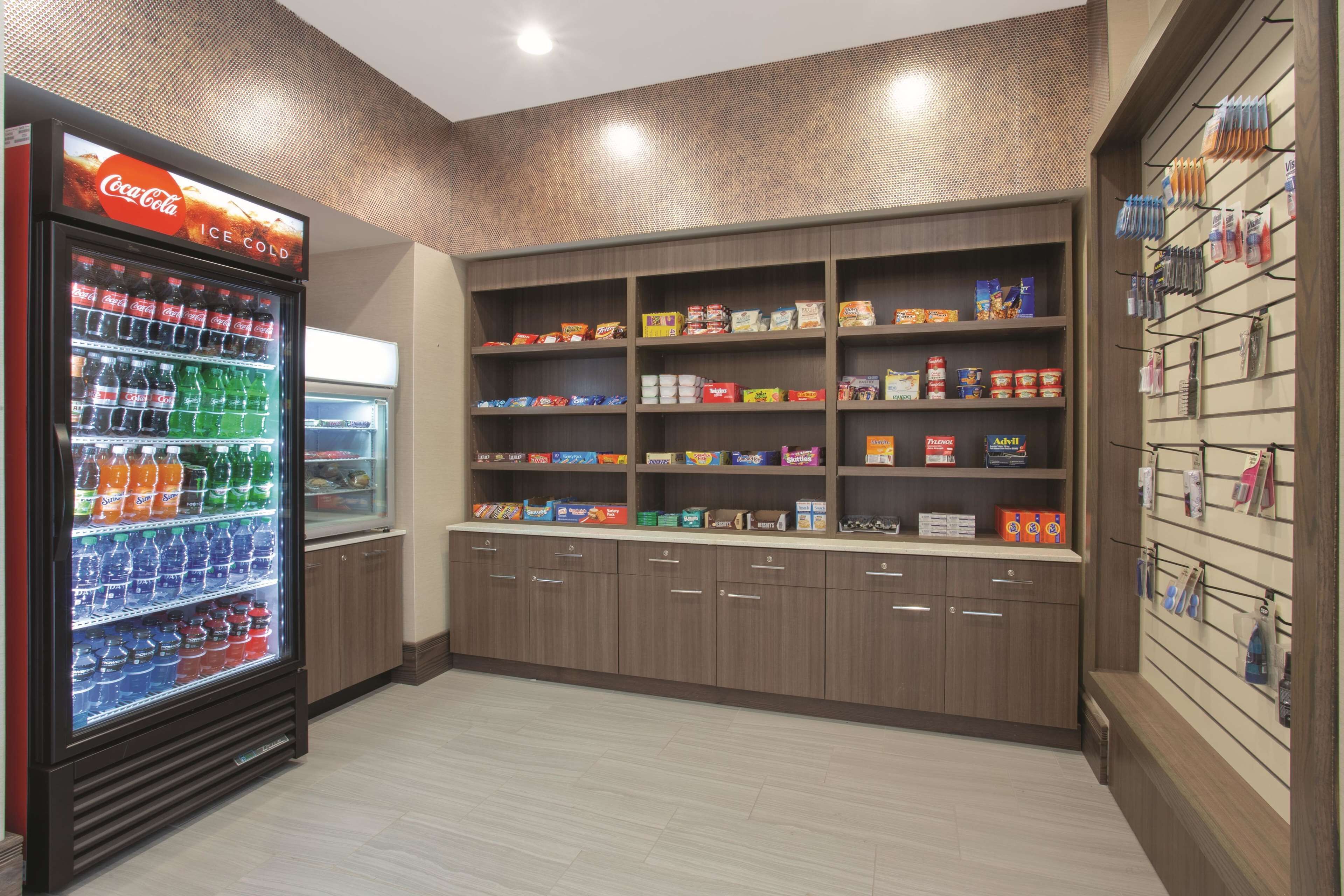 Un distributeur automatique orné d’une enseigne Coca-Cola, des étagères remplies de collations et de boissons, et un mur d’exposition où sont accrochés divers articles.