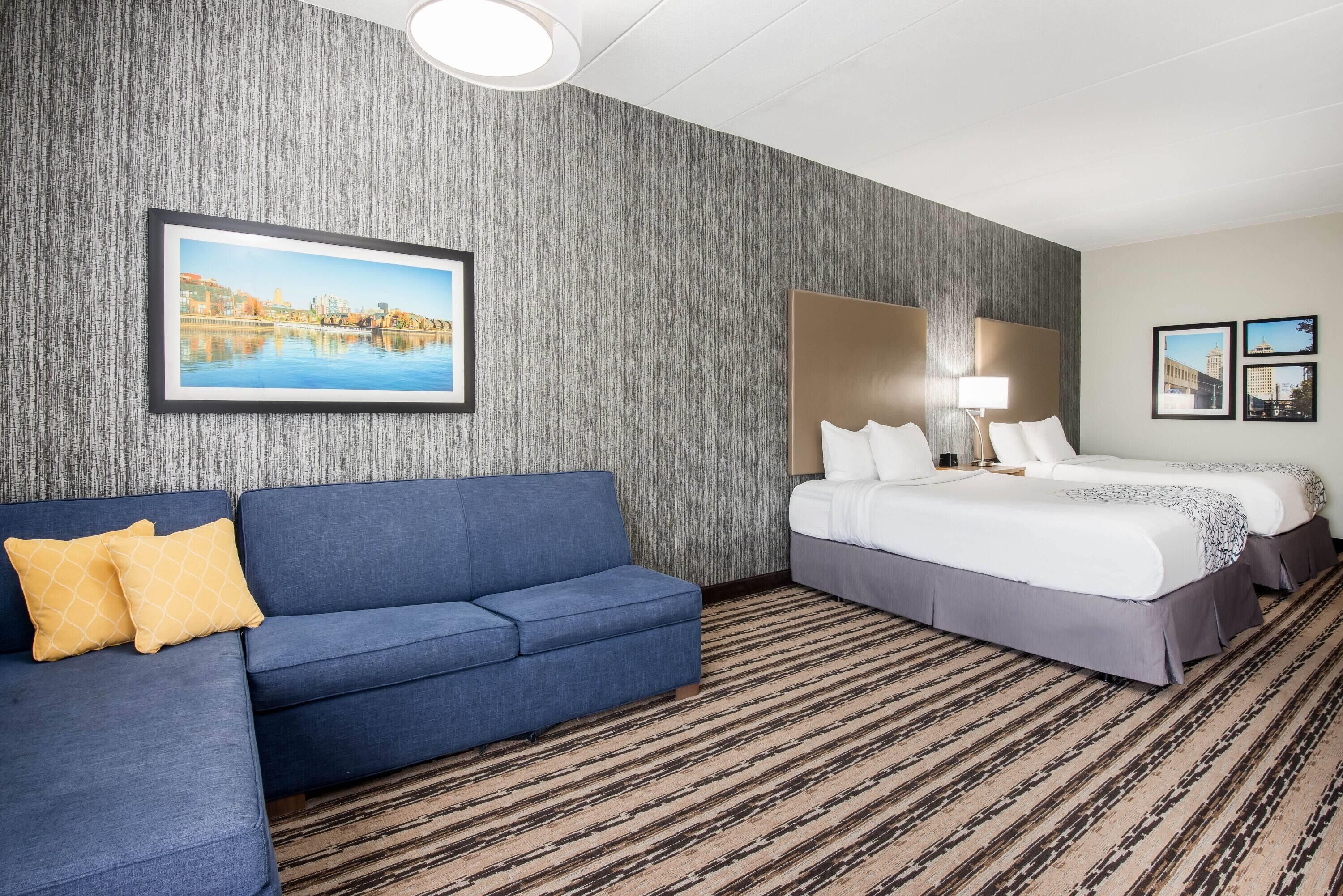 A hotel room with a large bed, a blue sofa, and a cityscape painting on the wall.