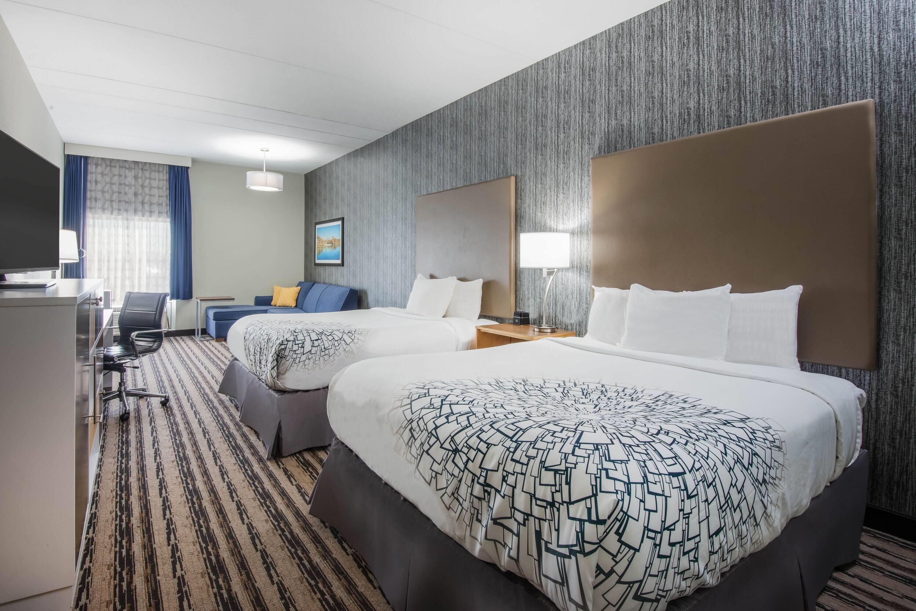 A hotel room with two beds, a desk, and a chair.