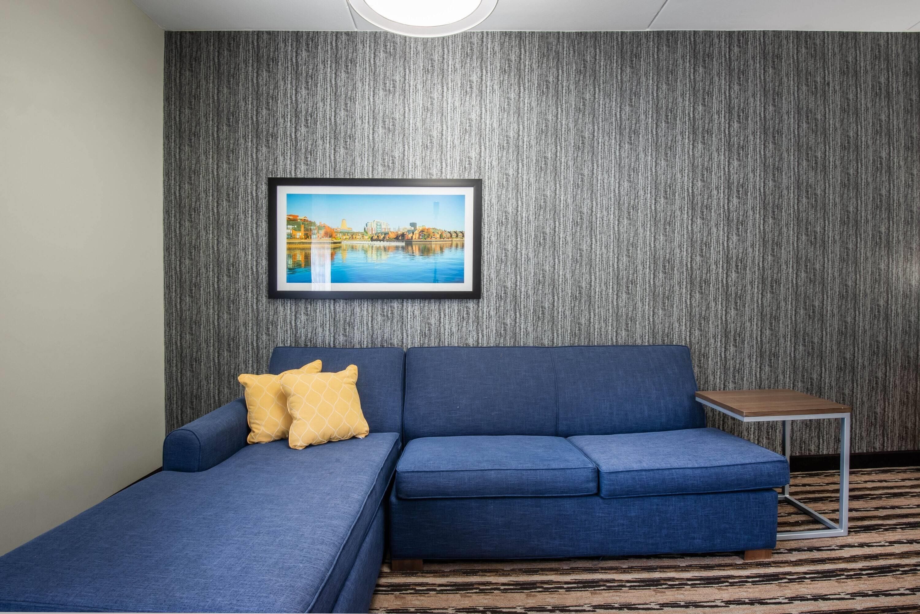 A room with a blue sofa, a small wooden side table, and a framed picture on the wall.