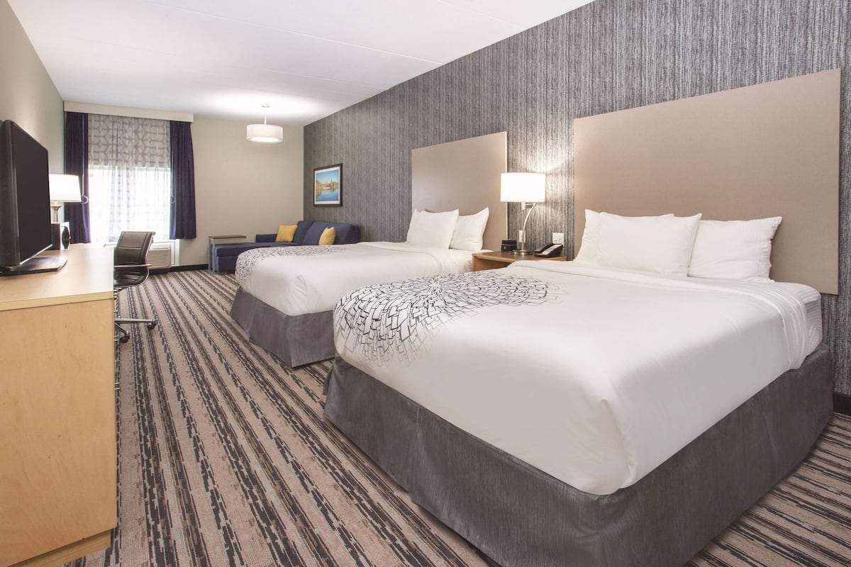 A hotel room with two beds, a desk, a chair, a TV, and a window with curtains.