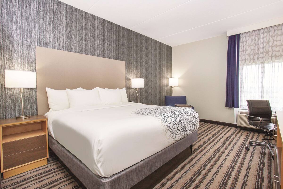 A hotel room with a large bed, two bedside lamps, a desk with a chair, and a patterned carpet.