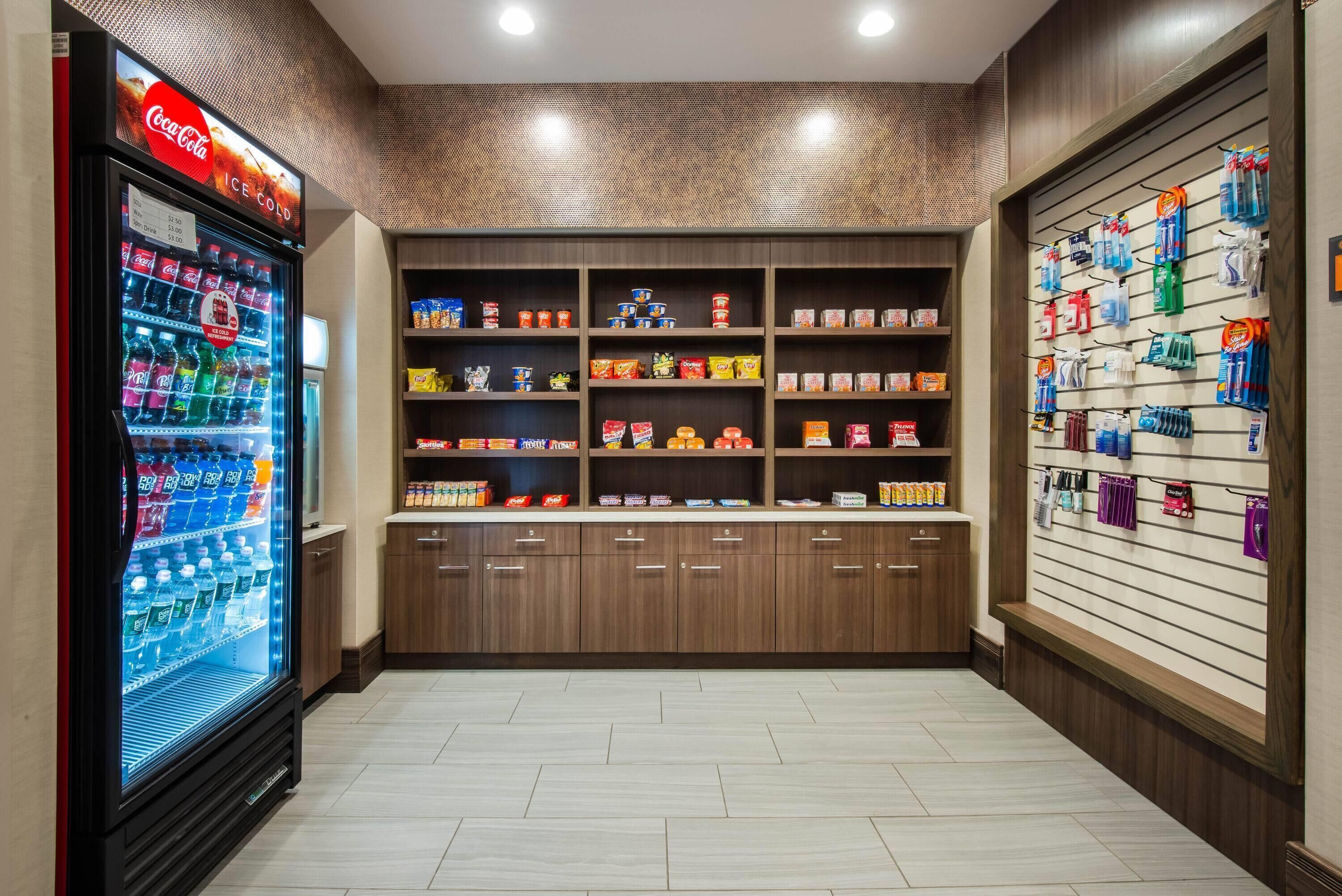 Een automatenruimte met een Coca-Cola koeler, planken vol snacks en een muur met diverse toiletartikelen.
