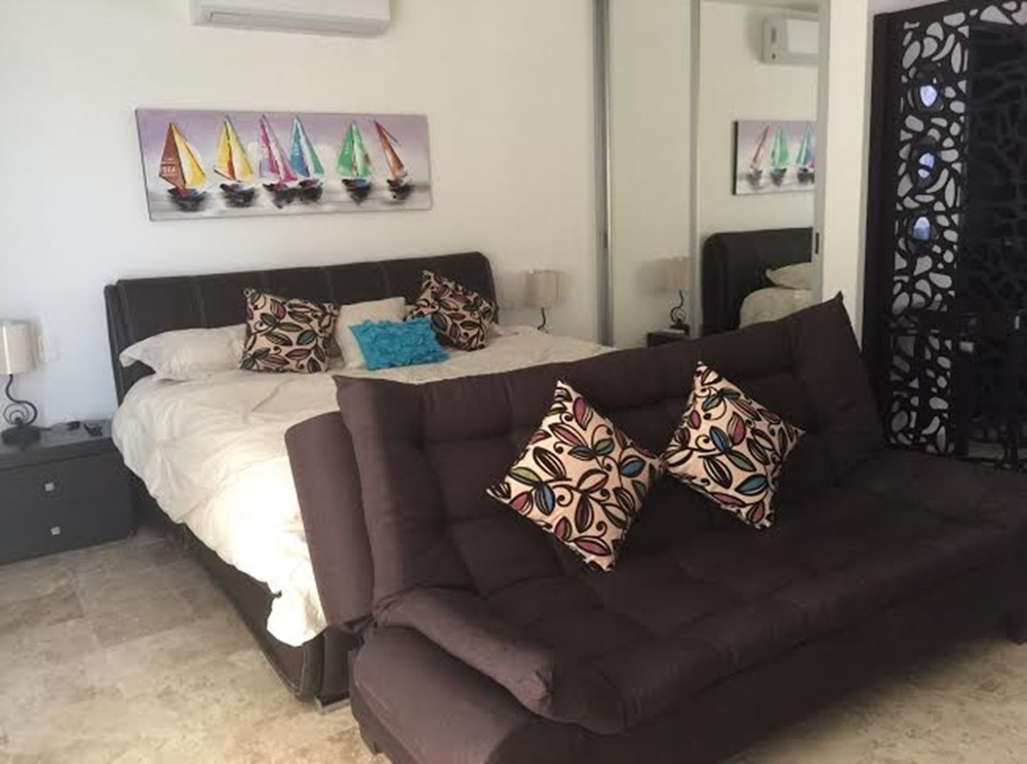 Un dormitorio con una cama, un sofá marrón oscuro y una pared decorada con pinturas de veleros.