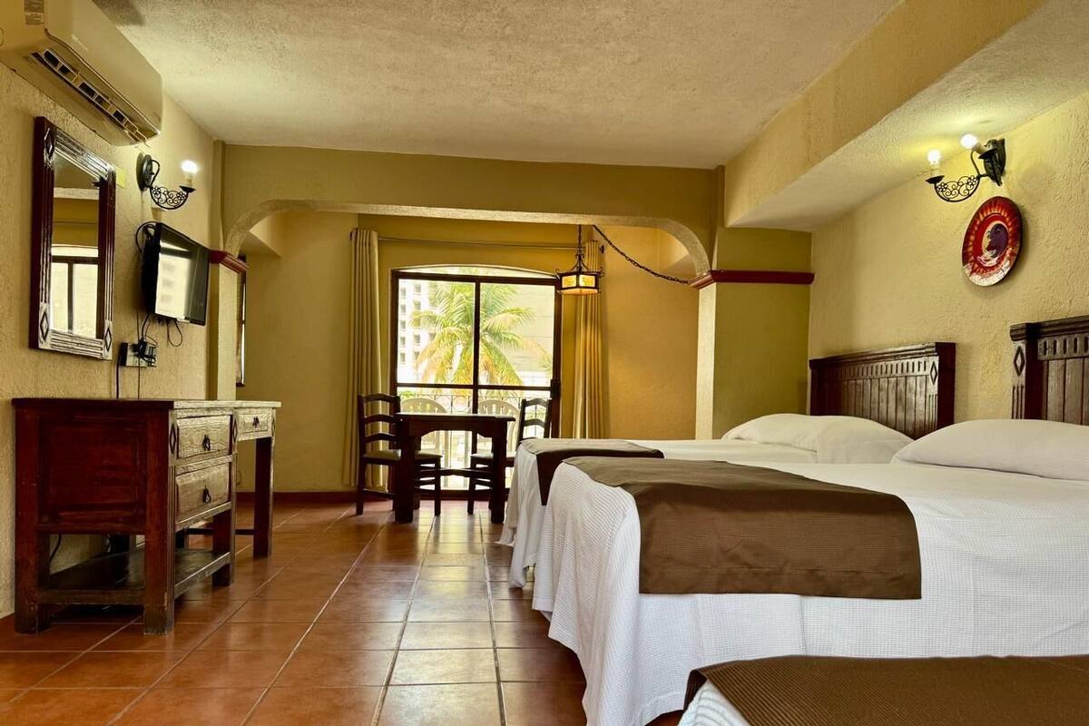 Une chambre d’hôtel avec deux lits, un bureau, une chaise, une télévision et une fenêtre avec des rideaux.