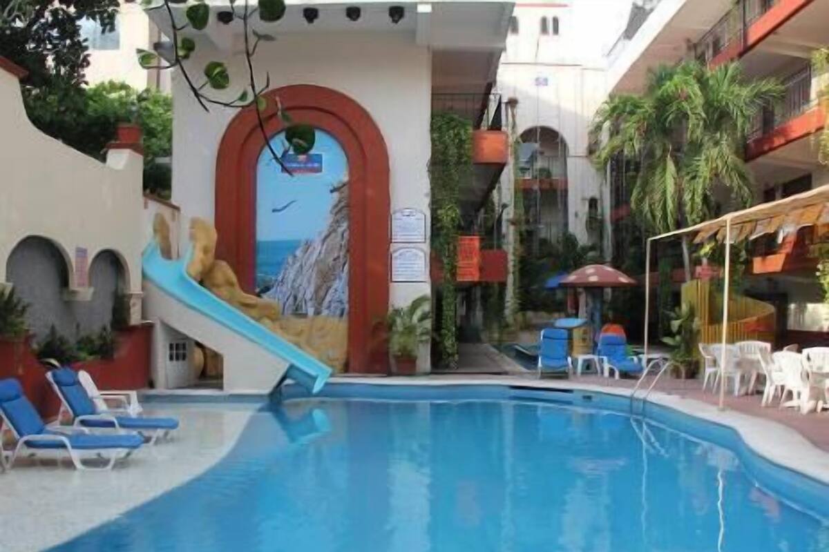 Une piscine avec un toboggan, des chaises longues et une vue sur un immeuble doté de balcons.