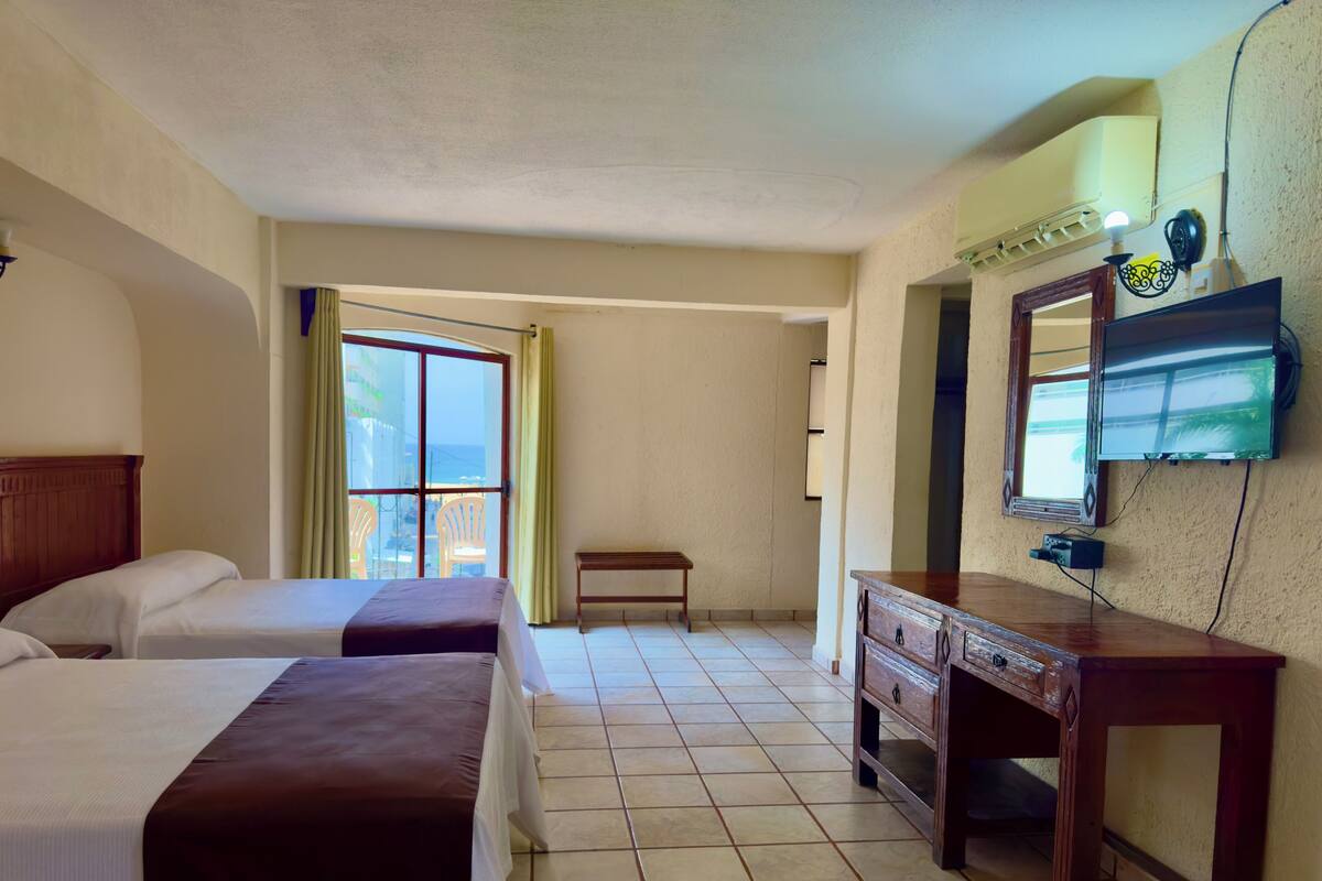 Une chambre d’hôtel avec deux lits, une commode en bois, un banc et un téléviseur fixé au mur.