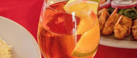 Un verre à cocktail, décoré d’une cerise, d’une tranche de citron vert et muni d’une paille, posé sur une nappe rouge.