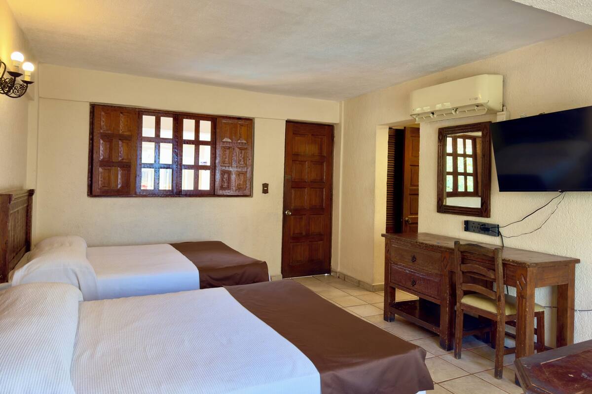 Une chambre d’hôtel avec deux lits, un bureau, une chaise, une télévision et une fenêtre avec des volets en bois.