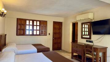A hotel room with two beds, a desk, a chair, a television, and a window with wooden shutters.