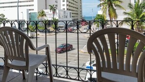 Varanda com duas cadeiras, vista para uma rua com carros e edifícios.