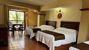Quarto de hotel com duas camas, uma mesa de jantar, cadeiras e vista para palmeiras através de uma janela grande.