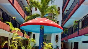 Piscina com um guarda-sol colorido, rodeada por vasos de plantas e um edifício com varandas.