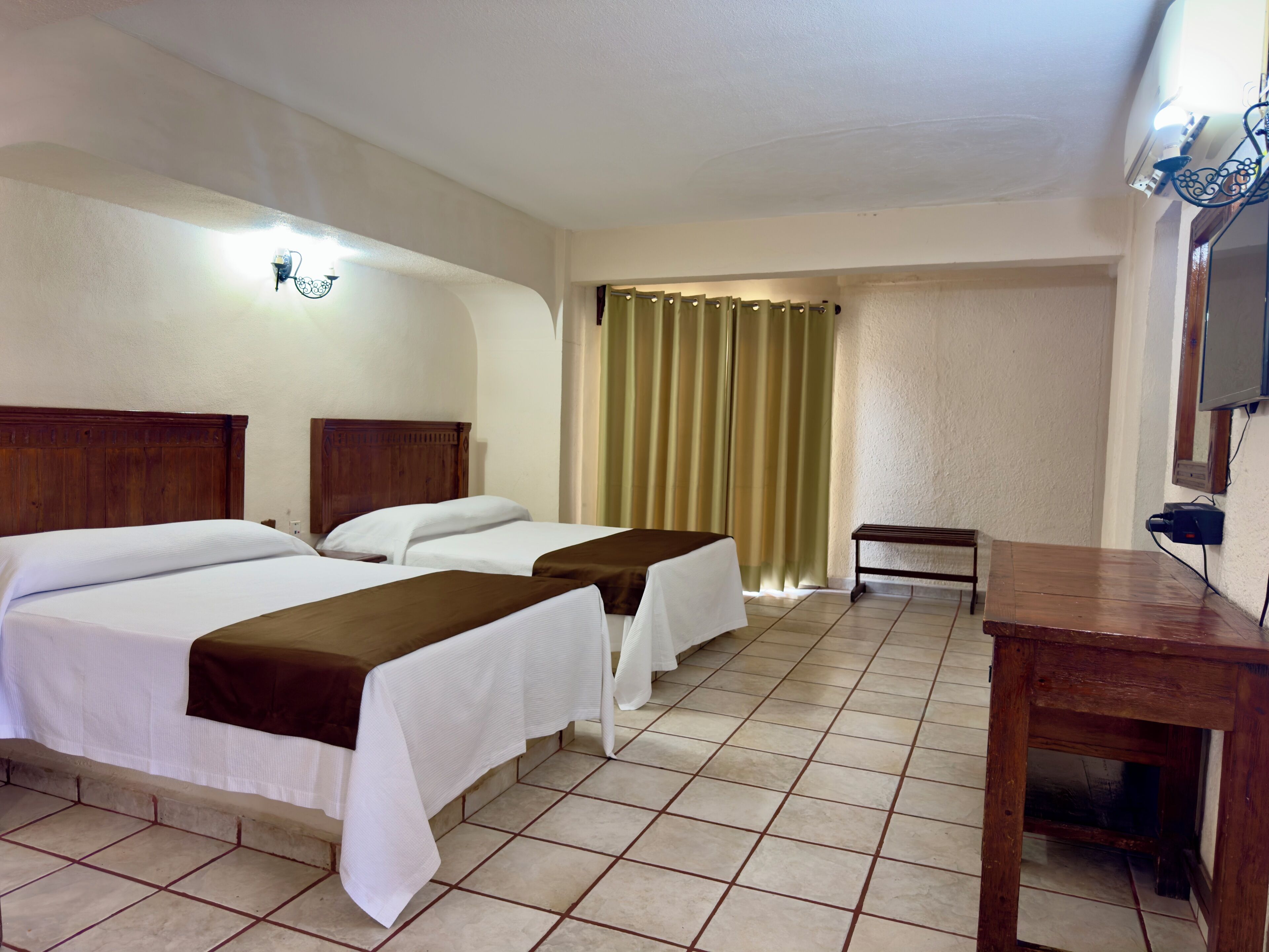 A hotel room with two beds, a wooden table, a TV, and a curtain.