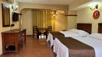 A hotel room with two beds, a wooden desk, a TV, and a dining table with chairs.