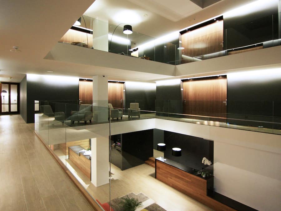 Um espaço de estar moderno, em vários níveis, com guarda-corpos de vidro, detalhes em madeira e mobiliário contemporâneo.